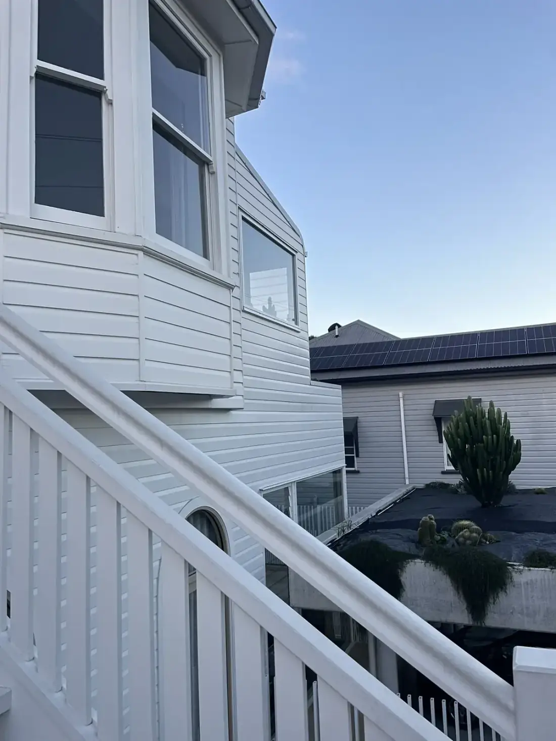 Queenslander timber facade with clean upper windows and rooftop solar panels next door